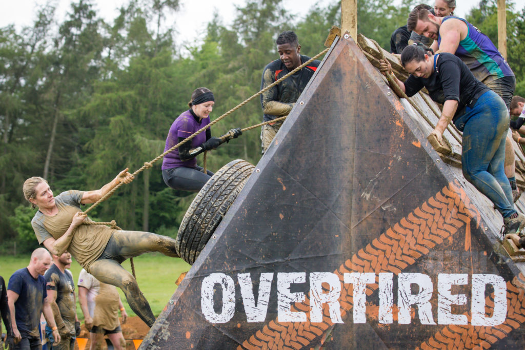 Several people climb an obstacle with a rope