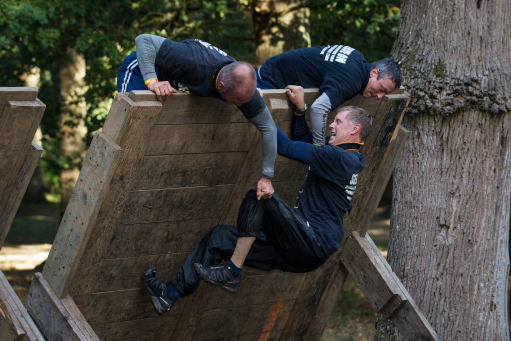 Two men pulling a third man over a tilted wall